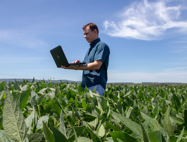 homem segurando notebook no meio de plantação